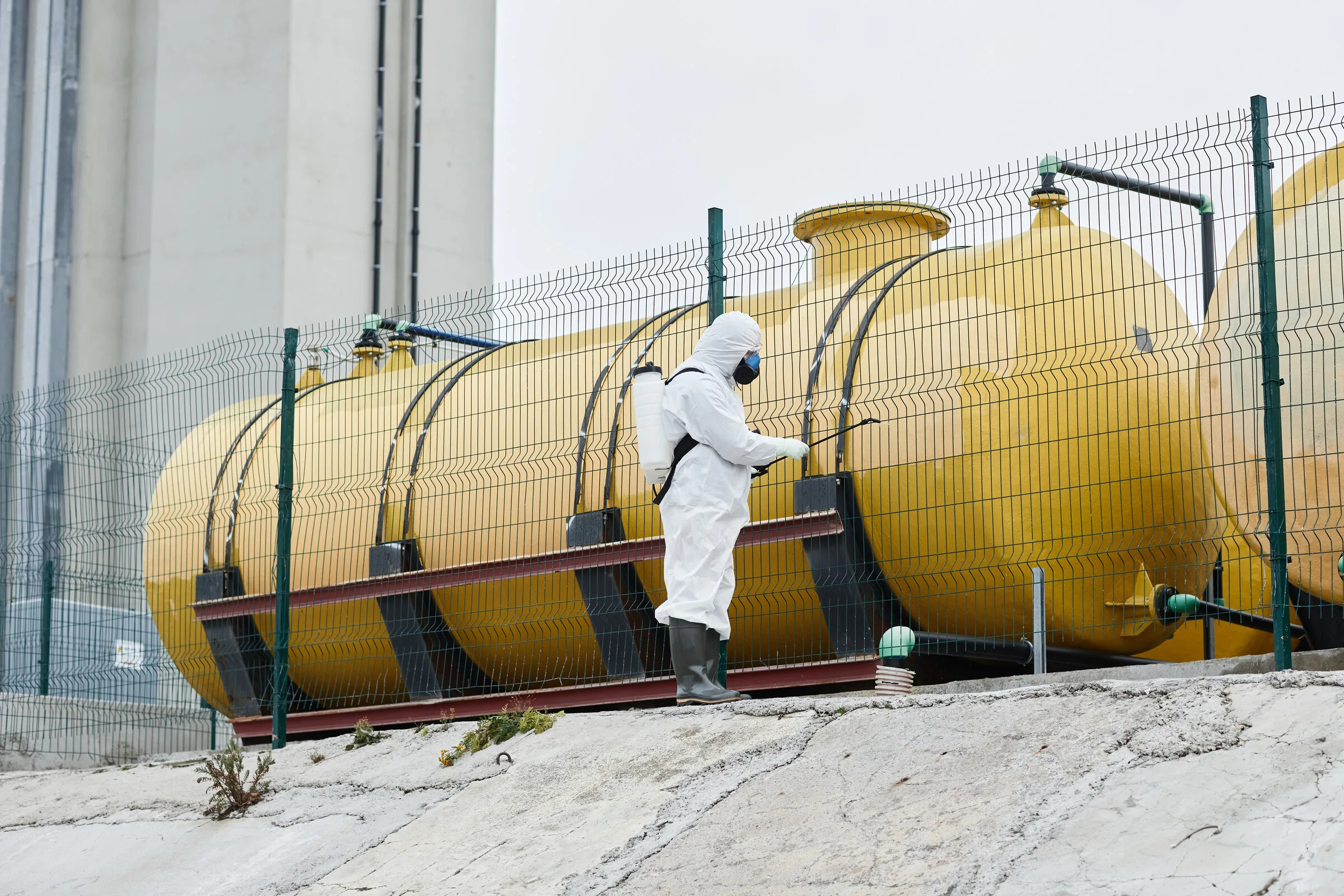 Worker in protective suit spraying an industrial tank