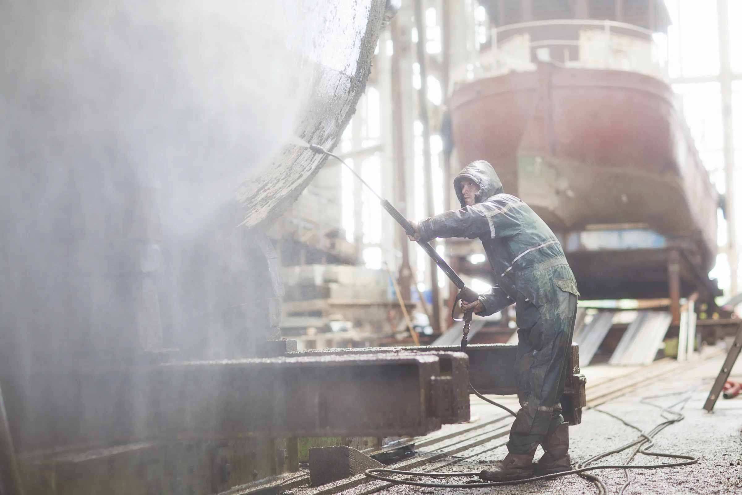 Worker pressure-washing a ship hull in dry dock