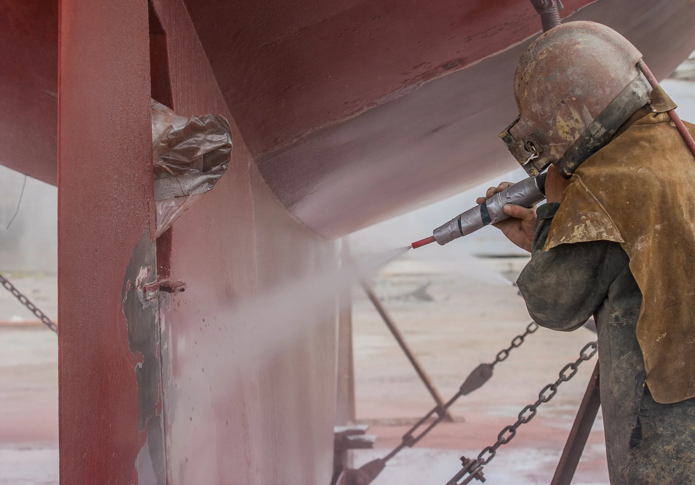 Worker sandblasting a ship hull for surface preparation