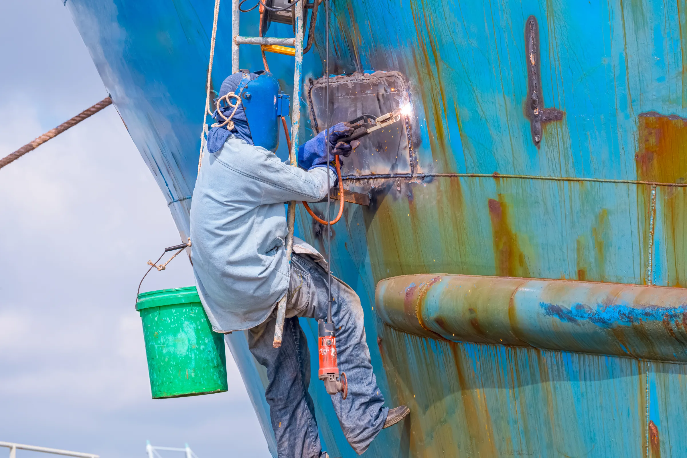 Shipyard worker welding a large boat section