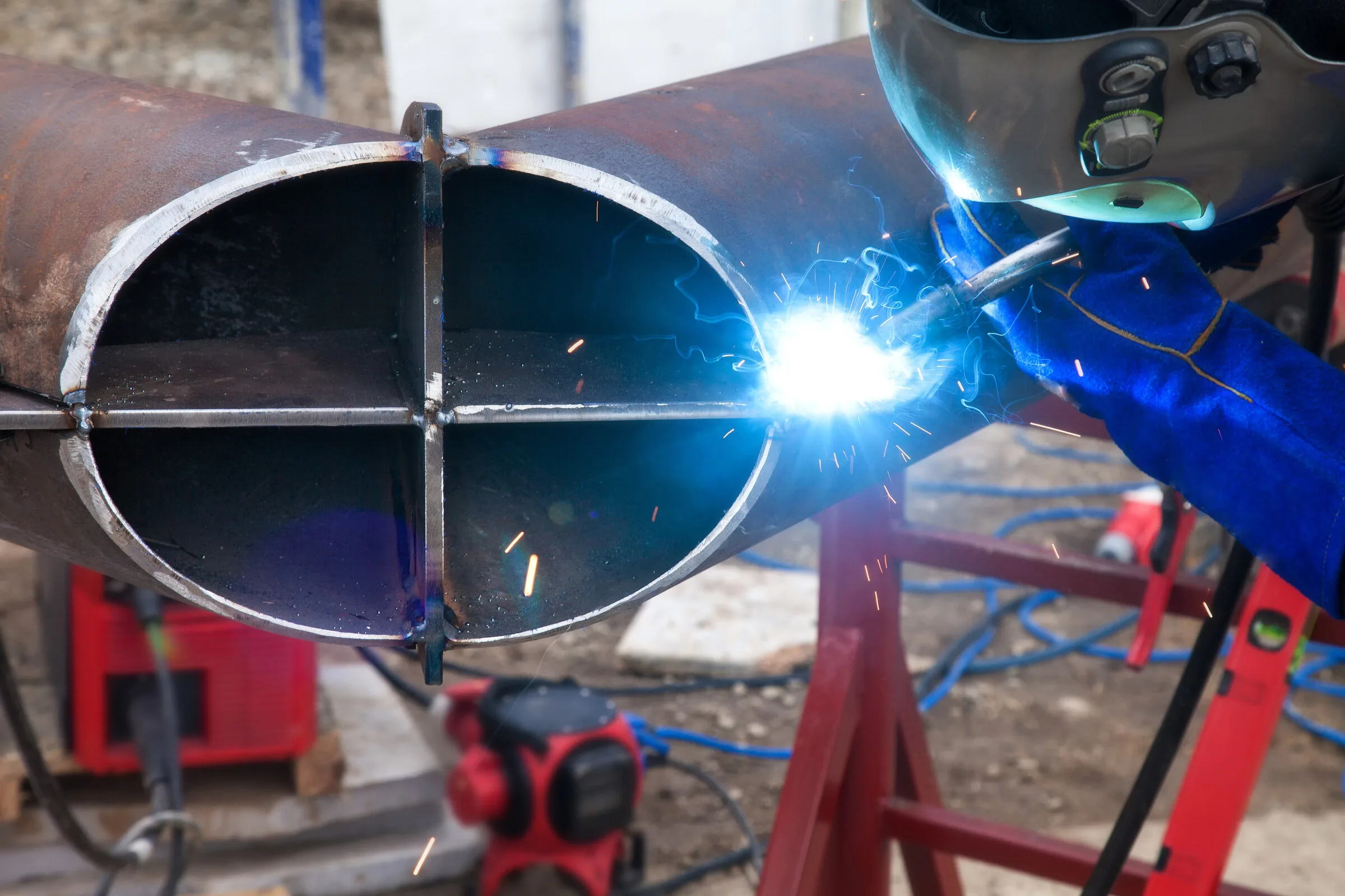 Welder joining a metal pipe with protective gear