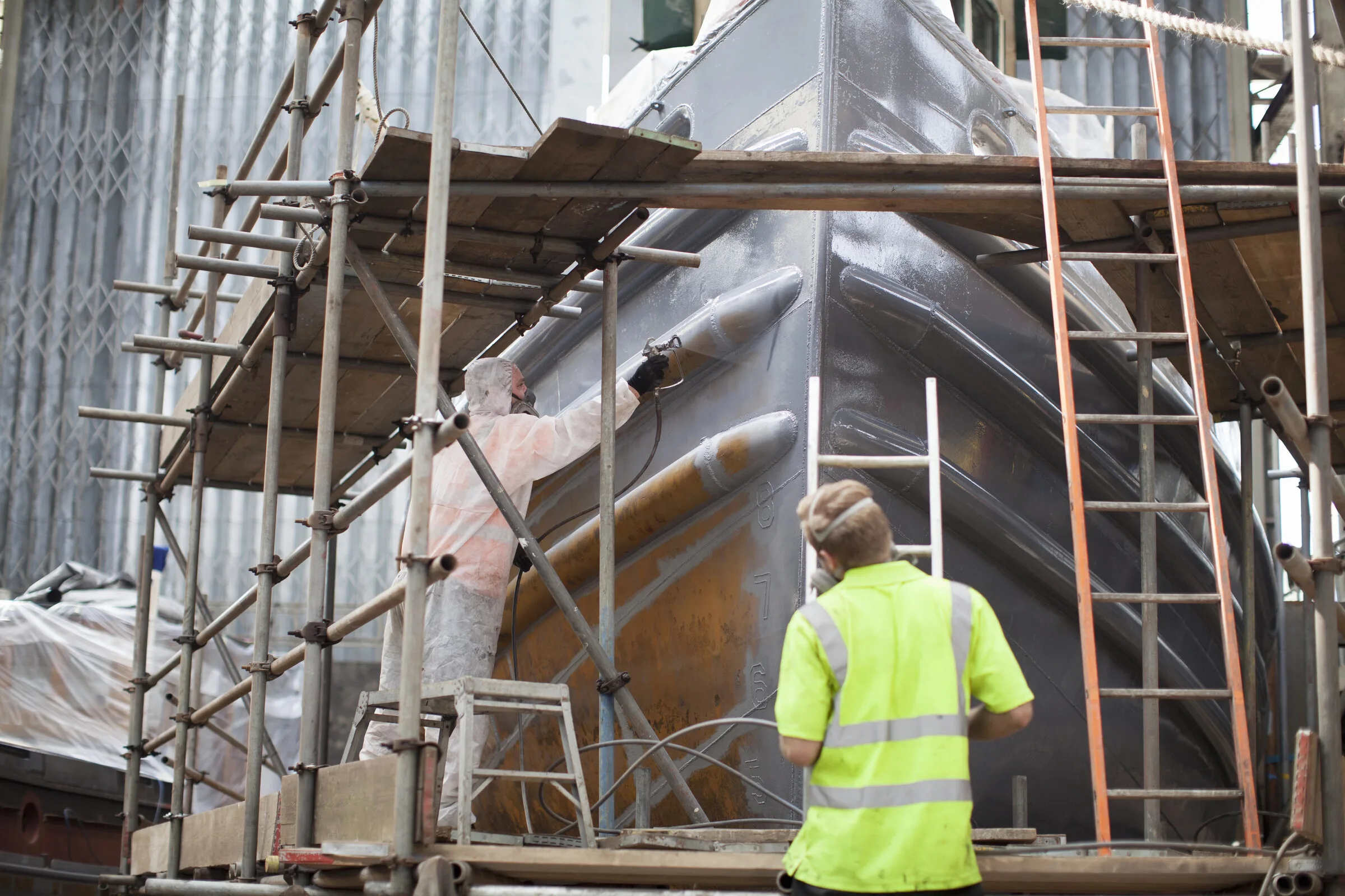 Workers painting a large metal object at an industrial site